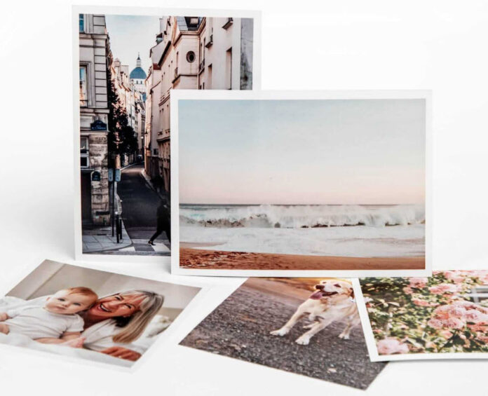 A collection of four Printique photographs scattered on a surface, depicting a city street, a beach scene, a smiling woman with a child, and a playful dog.