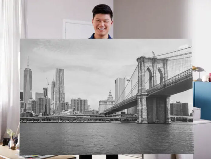 Man holding a large black-and-white photo print showing the Brooklyn Bridge and New York City skyline.